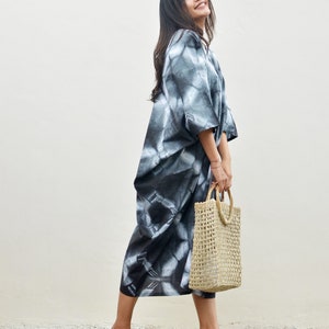 Puede incluir: Una mujer con un vestido maxi de tie-dye en blanco y negro, un bolso de mano de paja trenzada y sandalias de tac&oacute;n rosa.