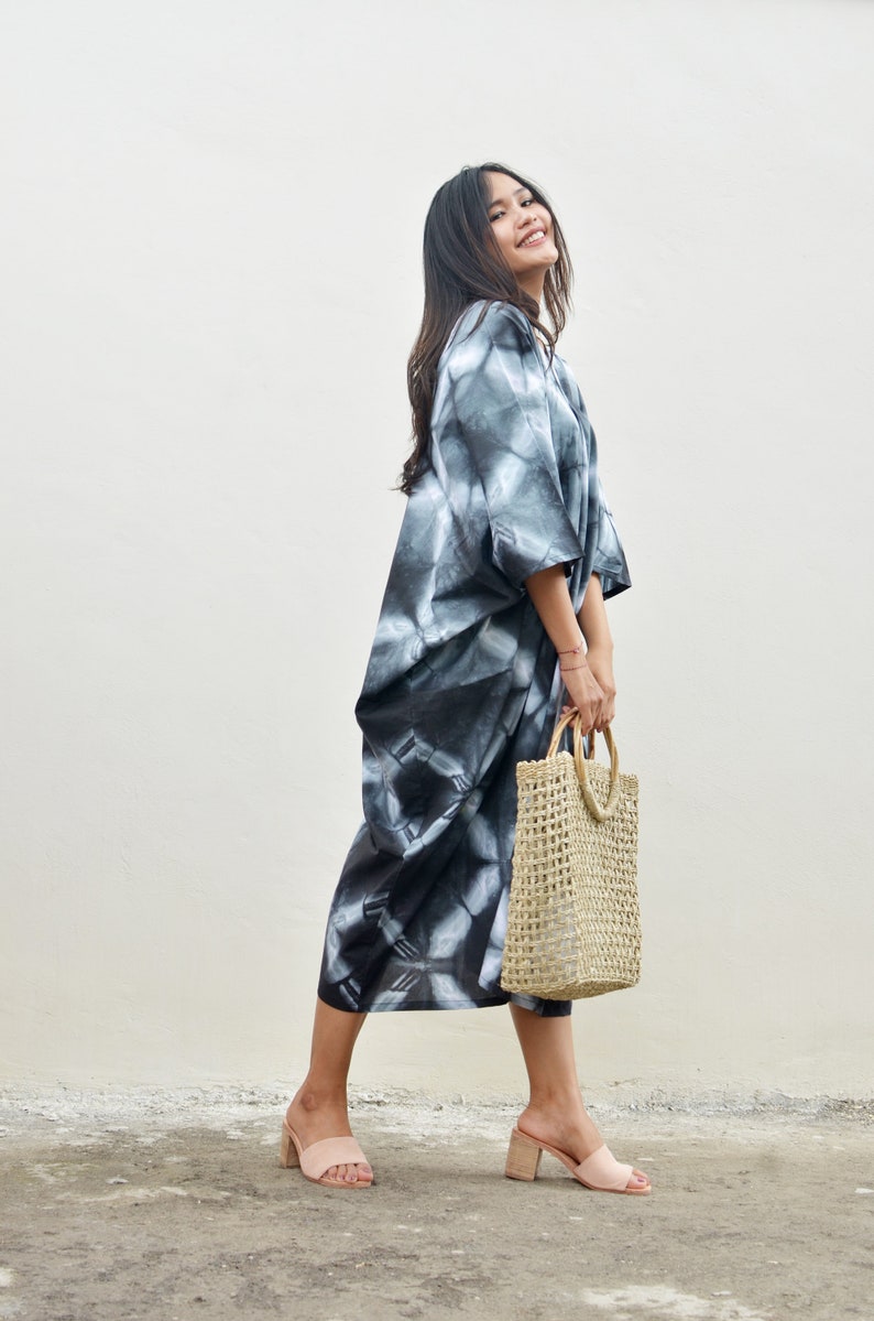 Puede incluir: Una mujer con un vestido maxi de tie-dye en blanco y negro, un bolso de mano de paja trenzada y sandalias de tac&oacute;n rosa.