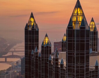May include: A view of several tall, black, glass skyscrapers with pointed tops. The buildings are illuminated by the setting sun, casting a warm glow on the city skyline.