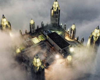 May include: An aerial view of a building with a glass roof and multiple towers, all covered in fog. The towers are shaped like pyramids and have windows that let in light. The building is surrounded by fog, giving it a mysterious and ethereal appearance.