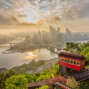 Peut inclure: Paysage urbain pittoresque au lever du soleil, avec un téléphérique rouge au premier plan. Le téléphérique, avec son toit et ses fenêtres rouges, se détache sur une ligne d'horizon urbaine reflétée dans la rivière.
