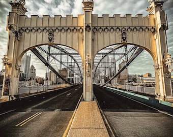 Könnte beinhalten: Eine weiße Brücke mit einem Stahlgerüst und zwei Türmen. Die Brücke führt über eine Straße mit gelben Linien. Die Brücke befindet sich in der Stadt und im Hintergrund sind Gebäude zu sehen.