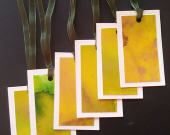 Könnte beinhalten: Sechs Aquarell-Lesezeichen in Grün- und Gelbtönen, jedes mit einem weißen Rand und einem Loch oben für ein Band. Die Bänder sind dunkelgrün.