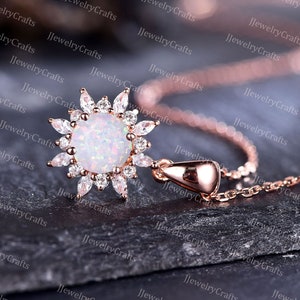 May include: A rose gold necklace with a white opal pendant surrounded by clear cubic zirconia stones. The pendant is shaped like a flower with a delicate chain.