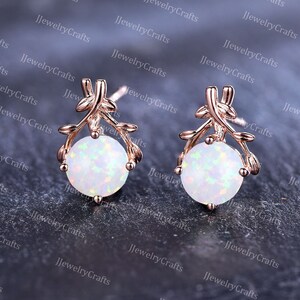 May include: A pair of rose gold earrings with a delicate branch design and a white opal gemstone in the center of each earring.