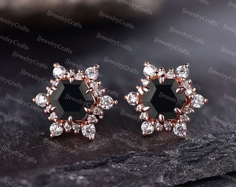 Könnte beinhalten: Ein Paar Ohrstecker aus Roségold mit einem schwarzen sechseckigen Edelstein, der von kleineren weißen Edelsteinen umgeben ist. Die Ohrringe haben ein schneeflockenartiges Design.