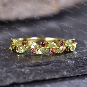 May include: A delicate gold band ring with a design of alternating green and red gemstones. The green gemstones are pear-shaped and the red gemstones are round.