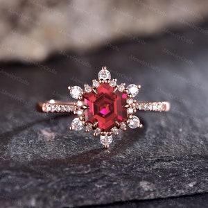 May include: A rose gold engagement ring with a large red hexagonal ruby gemstone surrounded by smaller white diamonds. The ring is set in a snowflake design.