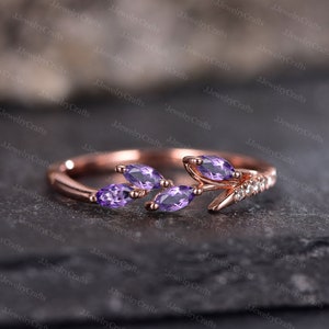 May include: A rose gold ring with a delicate branch design featuring four marquise-shaped amethyst gemstones. The branch is accented with small clear round stones.