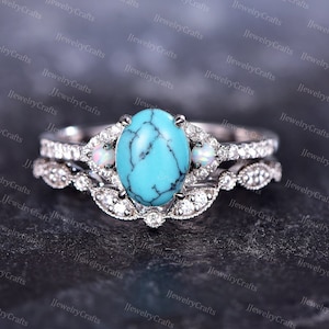 May include: A turquoise and opal engagement ring set with a silver band. The center stone is a large oval turquoise with a white opal on each side. The band is decorated with small diamonds.