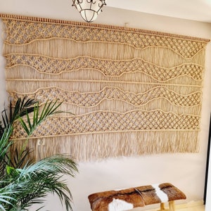 Jute wandkleed macramé met golvende lijnen. Zandkleurig modern wandkleed met zwevende lijnen