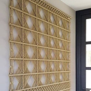 May include: A large, beige macrame wall hanging with a geometric diamond pattern and a fringe border.