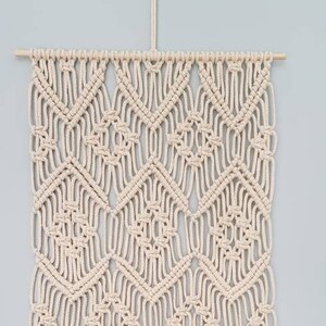 May include: A beige macrame wall hanging with a geometric pattern and a fringe border.