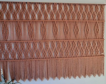 May include: A large macrame wall hanging with a geometric pattern in a warm brown color. The hanging has a fringe at the bottom.
