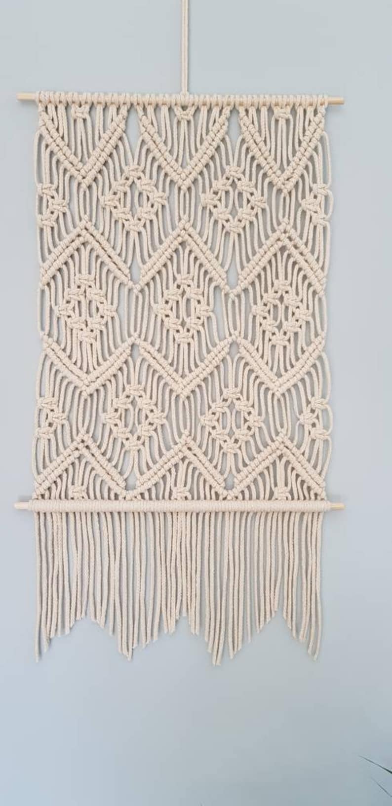 May include: A beige macrame wall hanging with a geometric pattern and a fringe border.