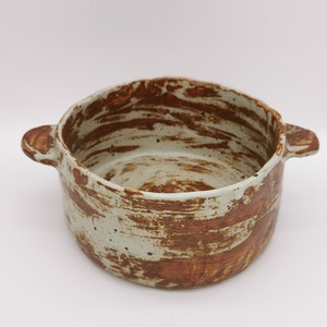 May include: A white ceramic baking dish with brown glaze and two handles. The dish has a rustic, handmade look.