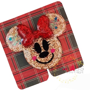 May include: A glittery Minnie Mouse-themed accessory with a red bow and gold glitter ears and face. The design is set against a red and black plaid background. The accessory has a black nose and eyes, and pink cheeks. The text "MYF BS BOUTIQUE" is visible.