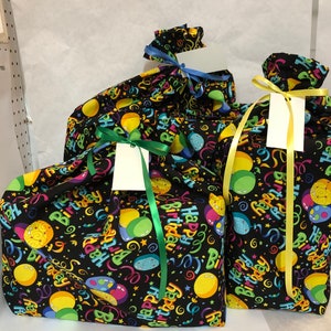 May include: Three black gift bags with colorful "Happy Birthday" print and balloons. The bags have green, yellow, and blue ribbons.