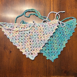 May include: Two handmade crochet bandanas. One is a mix of pastel colors, including pink, yellow, and blue. The other is a solid turquoise color. Both bandanas have a triangular shape with ties for securing around the neck.
