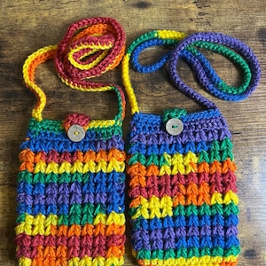 May include: Two rainbow crocheted phone pouches with matching straps. The pouches are made with a variety of colors, including red, orange, yellow, green, blue, and purple. Each pouch has a small button closure.