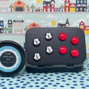 May include: A black tin with a white label that says "Pin Dreams On Magnetic Pins". The tin contains red and black magnetic pins with a Mickey Mouse design.