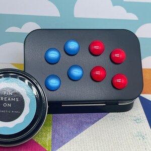May include: A black tin with a white label that says "Pin Dreams On - Magnetic Pins". The tin contains blue and red magnetic pins.