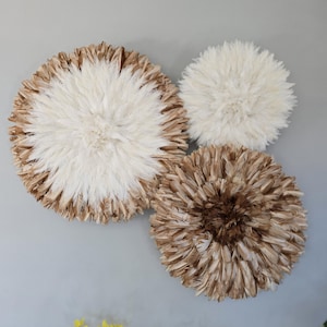 Peut inclure: Trois décorations murales rondes en plumes. La plus grande est blanche avec un bord marron. Les deux autres sont plus petites, l'une est blanche et l'autre est marron. Les décorations murales créent un effet doux et texturé.