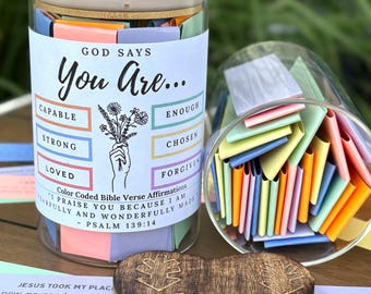 Könnte beinhalten: Ein Glas mit Holzdeckel, gefüllt mit farbenfrohen Affirmationskarten. Auf dem Glas steht "Gott sagt, du bist..." mit Wörtern wie "Fähig" und "Geliebt". Ein Holzherz und ein zweites Glas mit Karten sind ebenfalls zu sehen.