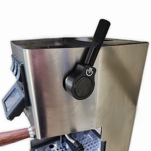 Op de afbeelding: Een espressomachine van roestvrij staal met een zwarte hendel en een houten handvat. De machine heeft een digitaal display en een druipbak.