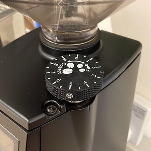 May include: A black coffee grinder with a dial that reads "Fine" to "Coarse" with a graphic of coffee beans. The dial is set to "Coarse".