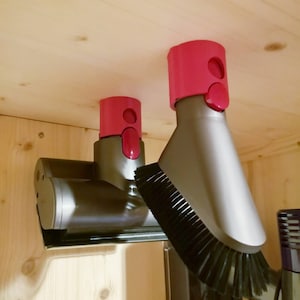 May include: Two gray vacuum cleaner attachments with pink plastic holders mounted on a wooden surface. The attachments have a brush and a nozzle.