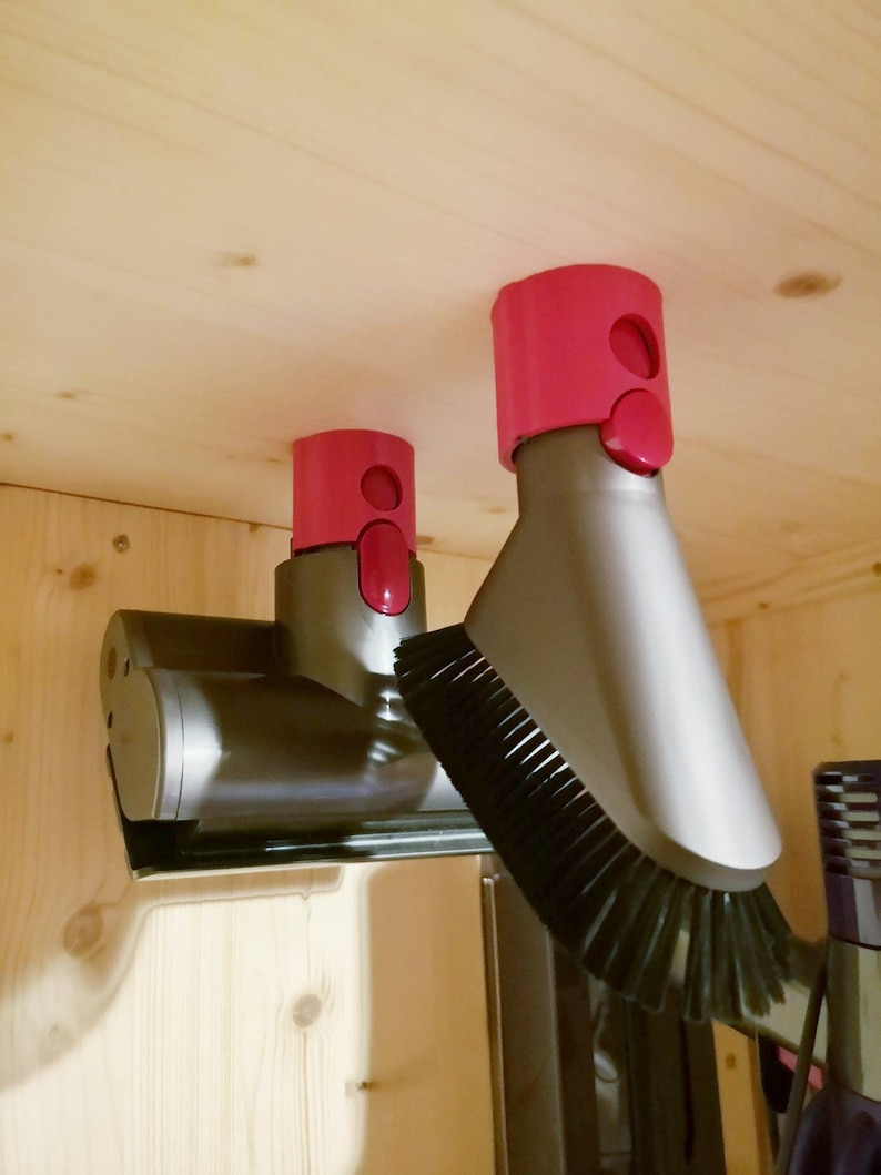 May include: Two gray vacuum cleaner attachments with pink plastic holders mounted on a wooden surface. The attachments have a brush and a nozzle.