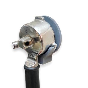 May include: A close-up of a silver and gray medical otoscope. The otoscope has a silver head with a gray rim and a black handle. The device is designed for examining the ear.