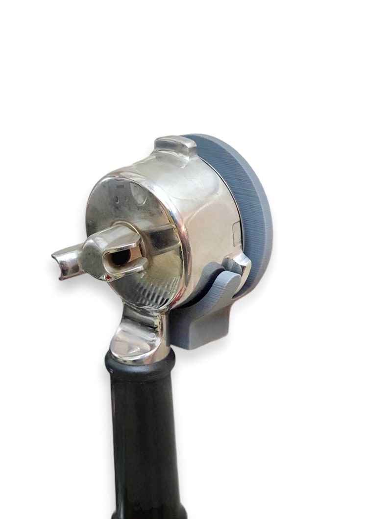 May include: A close-up of a silver and gray medical otoscope. The otoscope has a silver head with a gray rim and a black handle. The device is designed for examining the ear.