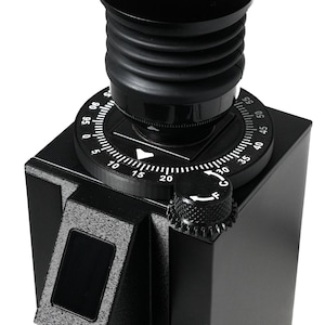 May include: A black coffee grinder featuring a top-mounted adjustment dial with numerical markings from 0 to 95, a ribbed cylindrical hopper lid, and a smaller side-mounted knob labeled with the letter F and a directional arrow for fine adjustment.