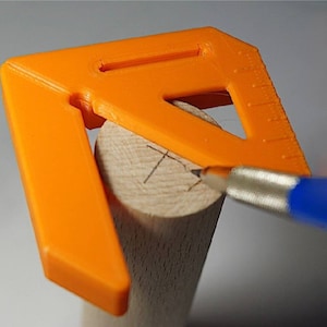 May include: An orange plastic woodworking tool with a ruler and a slot for a pencil. The tool is being used to mark a piece of wood.