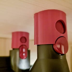 May include: Two pink plastic bottle stoppers with a round button on the side. The stoppers are on top of bottles.