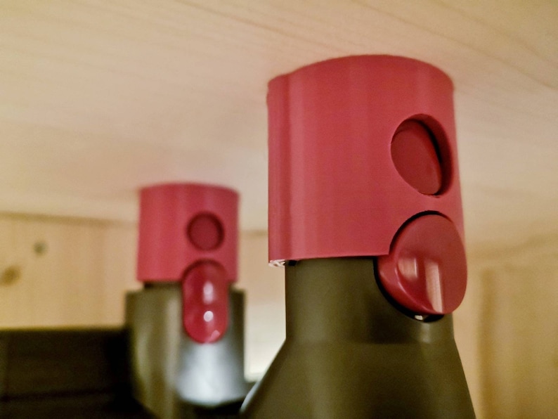 May include: Two pink plastic bottle stoppers with a round button on the side. The stoppers are on top of bottles.