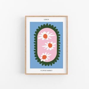 May include: A framed print with a blue background and a pink oval with three white flowers with orange centers. The oval is surrounded by a green border. The text "LISBON" and "FLOWER MARKET" are printed below the image.