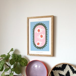 May include: A framed print with a blue background and a pink oval with three white flowers with orange centers. The oval is surrounded by a green border with a scalloped edge. The text "LINOCUT" is at the top of the print and "FLOWER MARKET" is at the bottom.