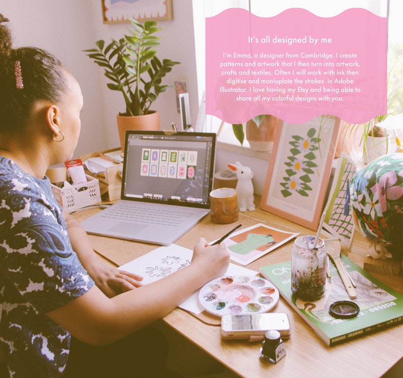 Op de afbeelding: Een vrouw zit aan een bureau en werkt aan een tekening met een penseel en een aquarelpalette. Ze heeft een laptop open voor zich, waarop een raster met kleurrijke ontwerpen te zien is. Achter haar hangen verschillende andere kleurrijke ontwerpen ingelijst aan de muur. De tekst "It's all designed by me" is in roze op een roze achtergrond geschreven.