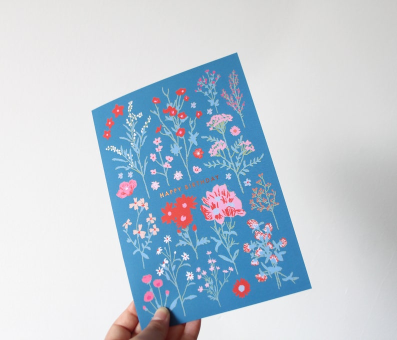 Op de afbeelding: Een blauwe kaart met een bloemenpatroon en de tekst "Happy Birthday" in gouden letters.