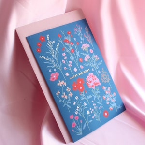 Op de afbeelding: Een blauwe kaart met een bloemenpatroon en de tekst "Happy Birthday" in gouden letters.