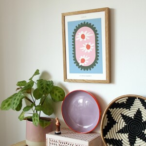 May include: A framed print with a pink and green floral design. The print is titled "London" and "Elizabeth Market". The print is hanging on a white wall above a wooden crate.
