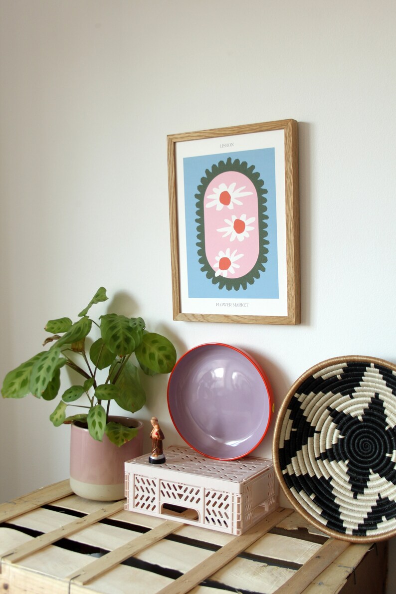 May include: A framed print with a pink and green floral design. The print is titled "London" and "Elizabeth Market". The print is hanging on a white wall above a wooden crate.