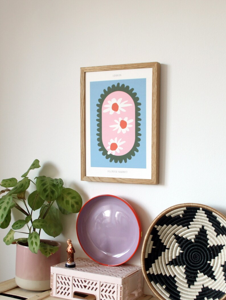 May include: A framed print with a blue background and a pink oval with three white flowers with orange centers. The oval is surrounded by a green border with a scalloped edge. The text "LINOCUT" is at the top of the print and "FLOWER MARKET" is at the bottom.