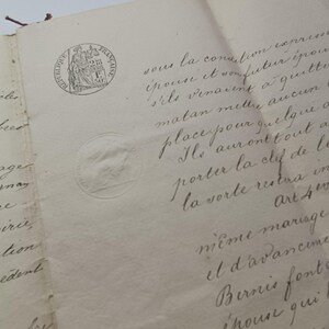 Może przedstawiać: Zbliżenie na antyczny dokument z odręcznym tekstem w wyblakłym tuszu. Papier jest postarzany i nosi ślady zużycia. Widoczne są dwie okrągłe pieczęcie, jedna ze szczegółowym herbem, a druga z prostym wzorem. Dokument historyczny.