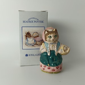 May include: A ceramic figurine of a cat from The World of Beatrix Potter collection. The cat is wearing a pink bonnet, blue vest, and green skirt. The figurine is holding a basket. The box behind the figurine has the text "The World of Beatrix Potter" and "Royal Albert".
