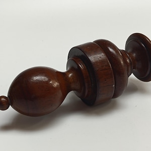 Peut inclure: Un bouchon de bouteille en bois brun foncé. Il présente une extrémité arrondie, une série de sections cylindriques et un dessus circulaire. Le bois a une finition polie et brillante. Mesure environ 15 cm de long.