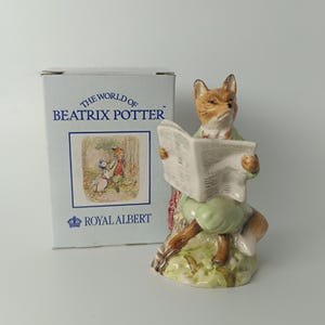 May include: A ceramic figurine of a fox reading a newspaper, wearing a green jacket and pants. The figurine is part of the "World of Beatrix Potter" collection by Royal Albert. A box with the same branding is behind the figurine.